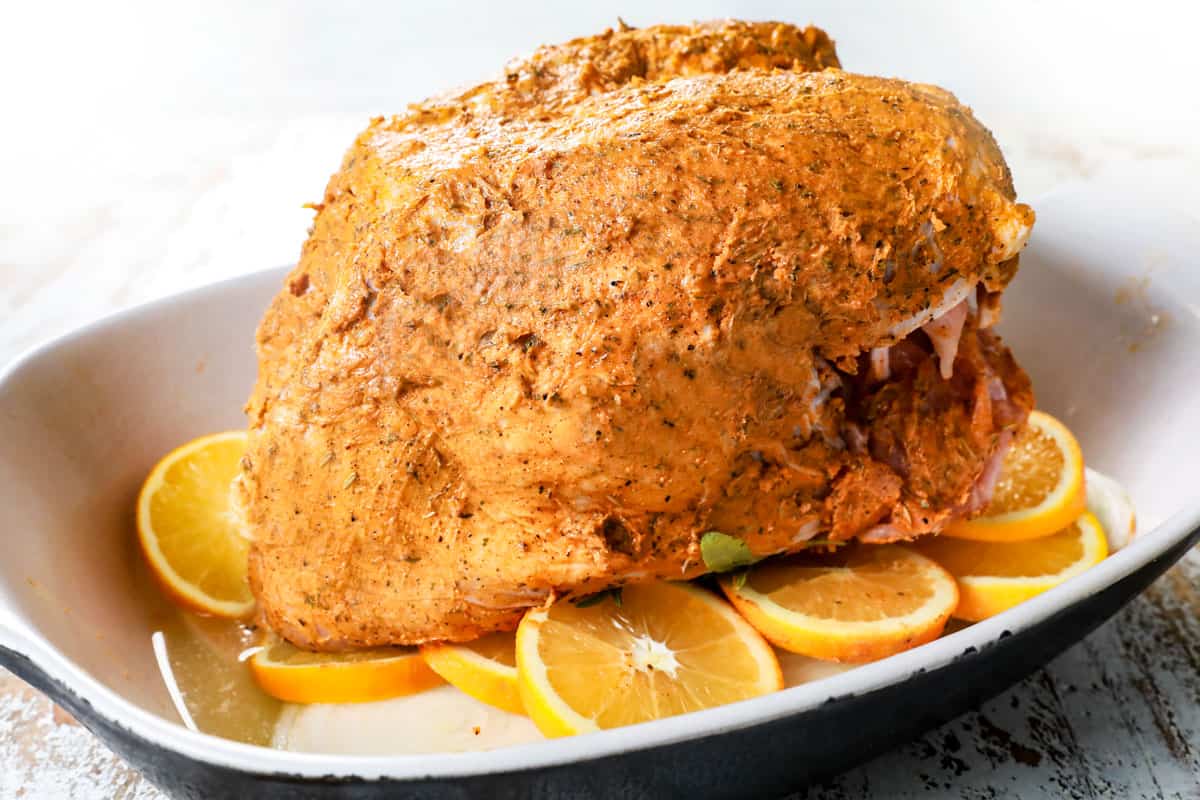showing how to make roast turkey breast by roasting the turkey in a roasting pan on top of onions and oranges