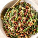 showing how to serve Green Beans Almondine by adding to a bowl and garnishing with bacon
