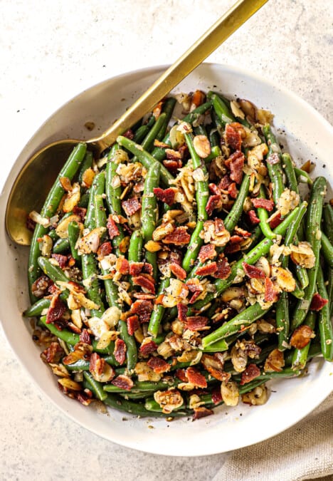 showing how to serve Green Beans Almondine by adding to a bowl and garnishing with bacon