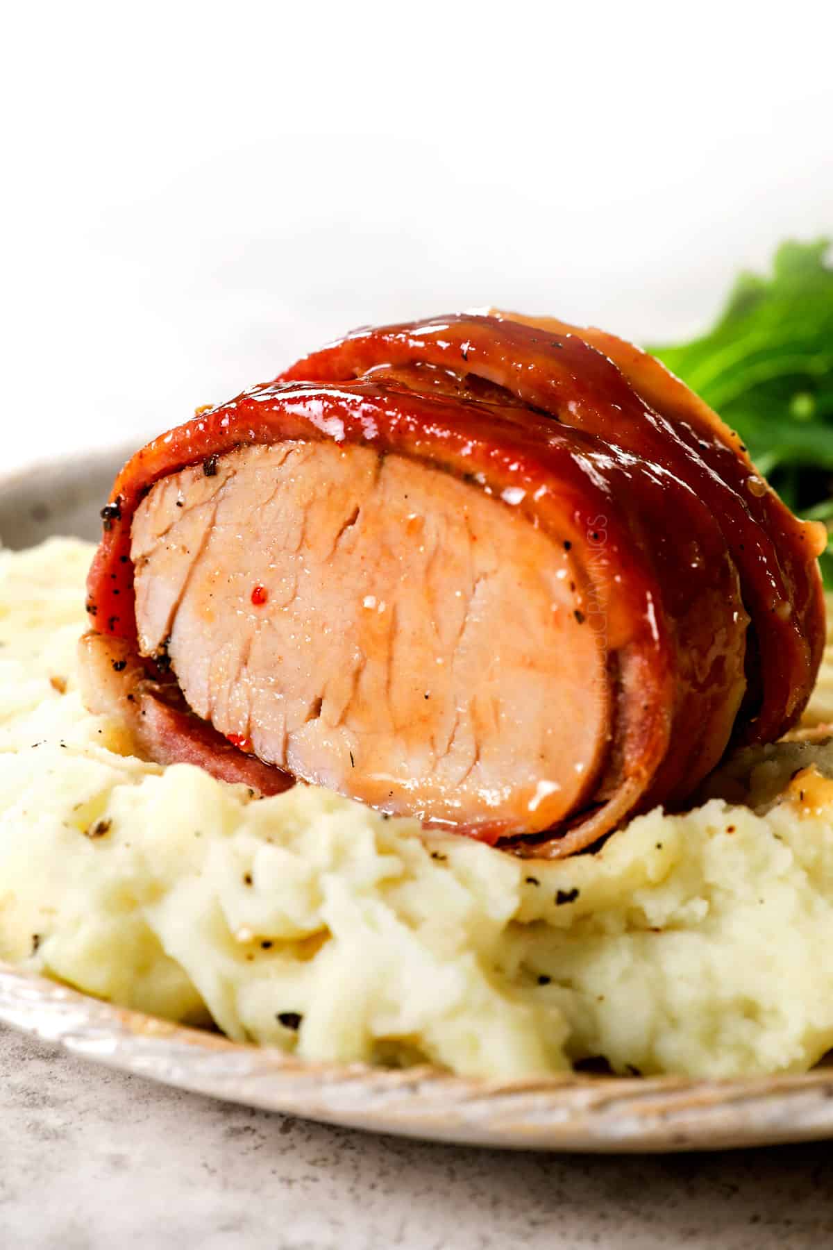 showing how to serve bacon-wrapped pork tenderloin by serving with mashed potatoes and vegetables