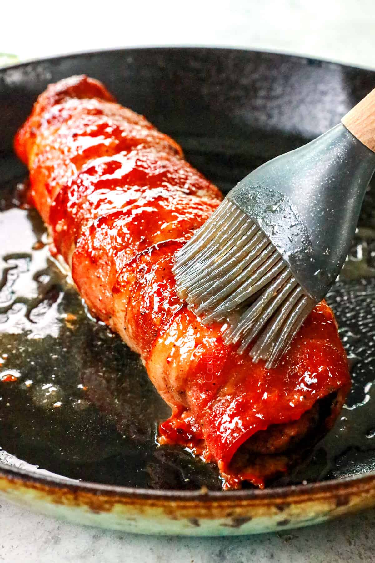 showing how to make bacon wrapped pork tenderloin by brushing the pork with glaze after baking