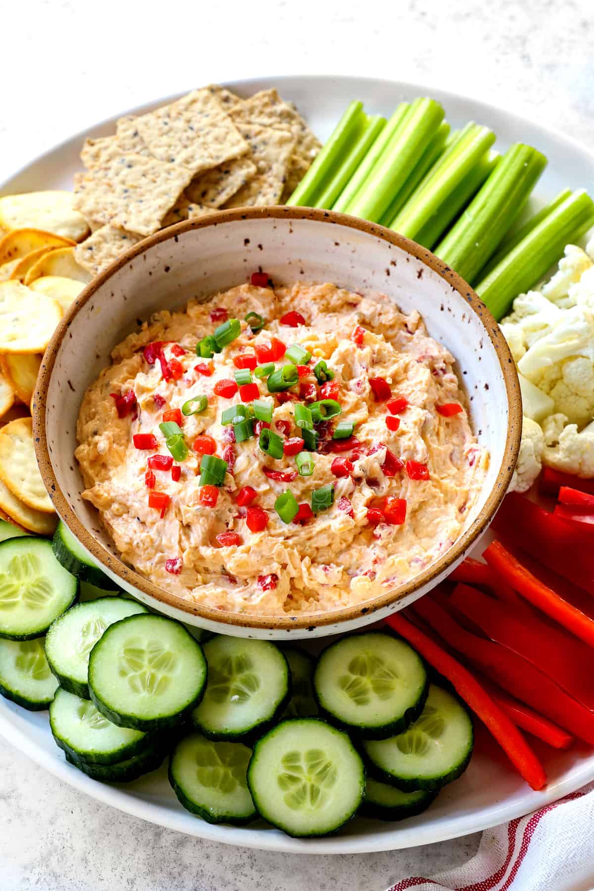 showing how to serve pimento cheese recipe adding to a platter with cucumbers, celery, bell peppers, cauliflower and crackers