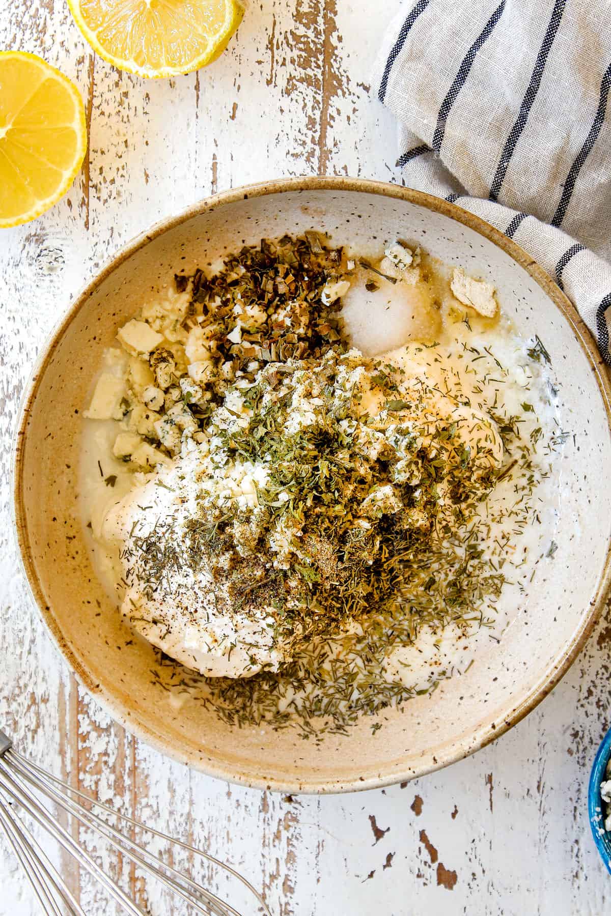showing how to make blue cheese dressing by whisking blue cheese, mayonnaise, Greek yogurt, chives, parsley, dill, garlic powder, onion powder, salt and pepper together in a bowl
