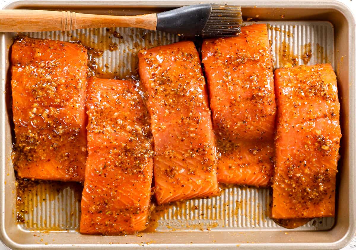 showing how to make baked honey mustard salmon by brushing the salmon with the marinade