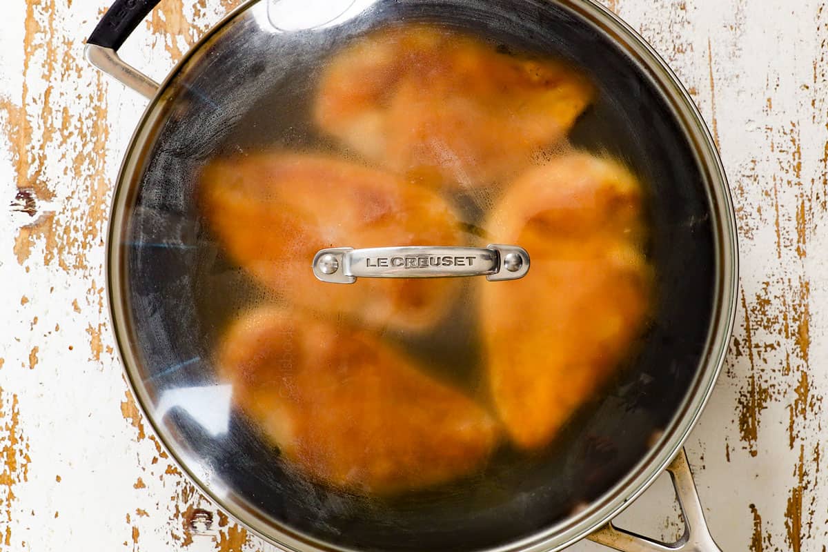 showing how to make shredded chicken by adding chicken broth to the chicken in a pan, covering and steaming