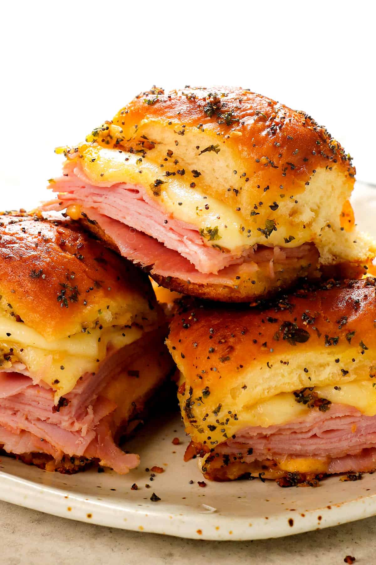 a stack of baked hot ham and cheese sliders on Hawaiian rolls, ham and Swiss cheese on a plate showing how to serve