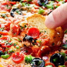 up close of scooping up baked pizza dip with a baguette slice