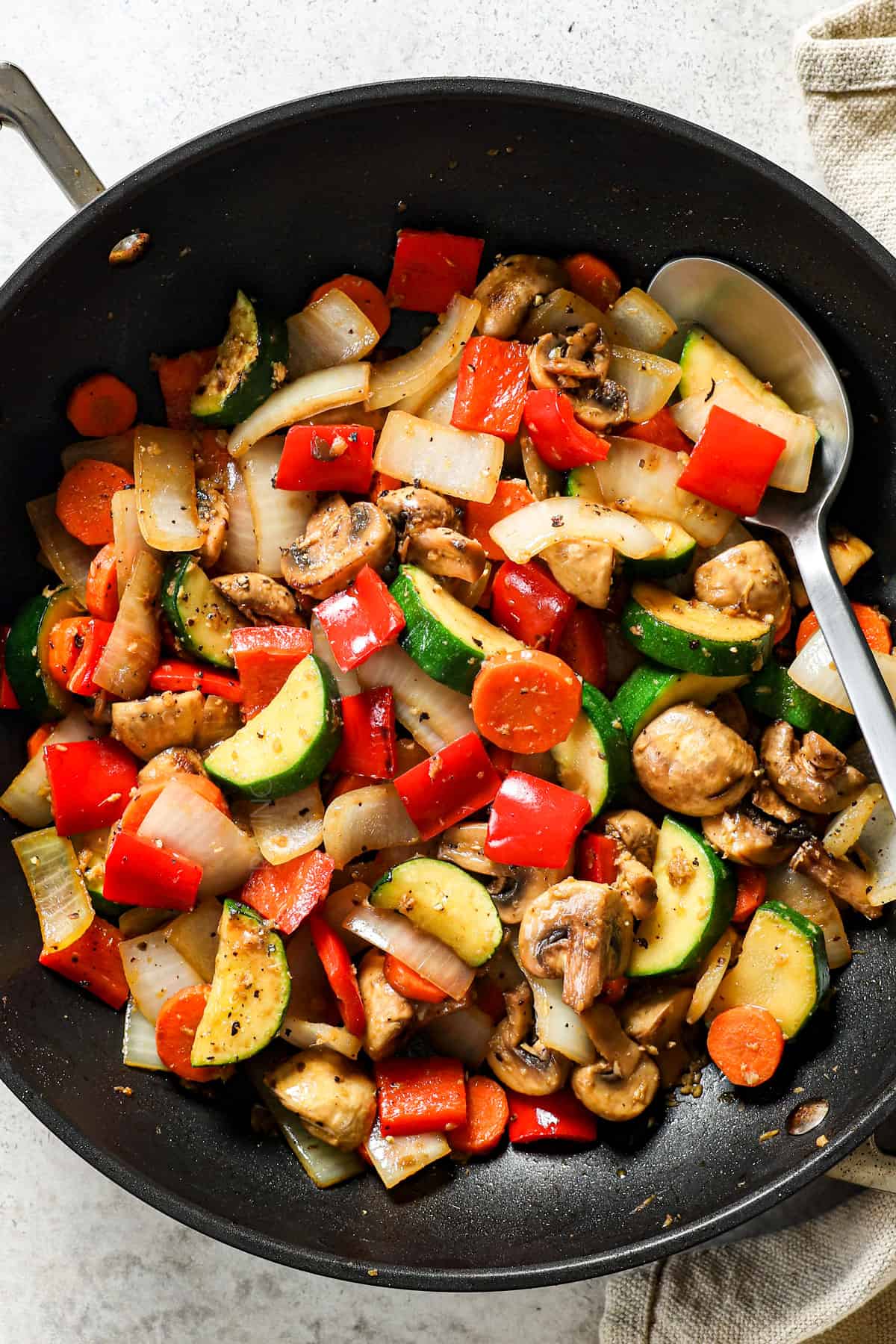 showing how to make chicken hibachi by adding carrots, zucchini, bell peppers and onions to a skillet to stir fry