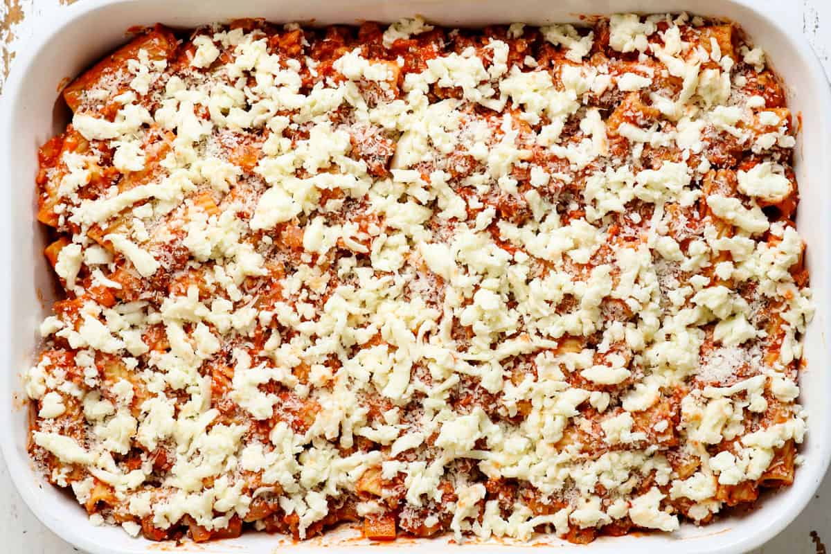 showing how to make baked rigatoni recipe (rigatoni al forno) by adding mozzarella and Parmesan to the top of the pasta before baking