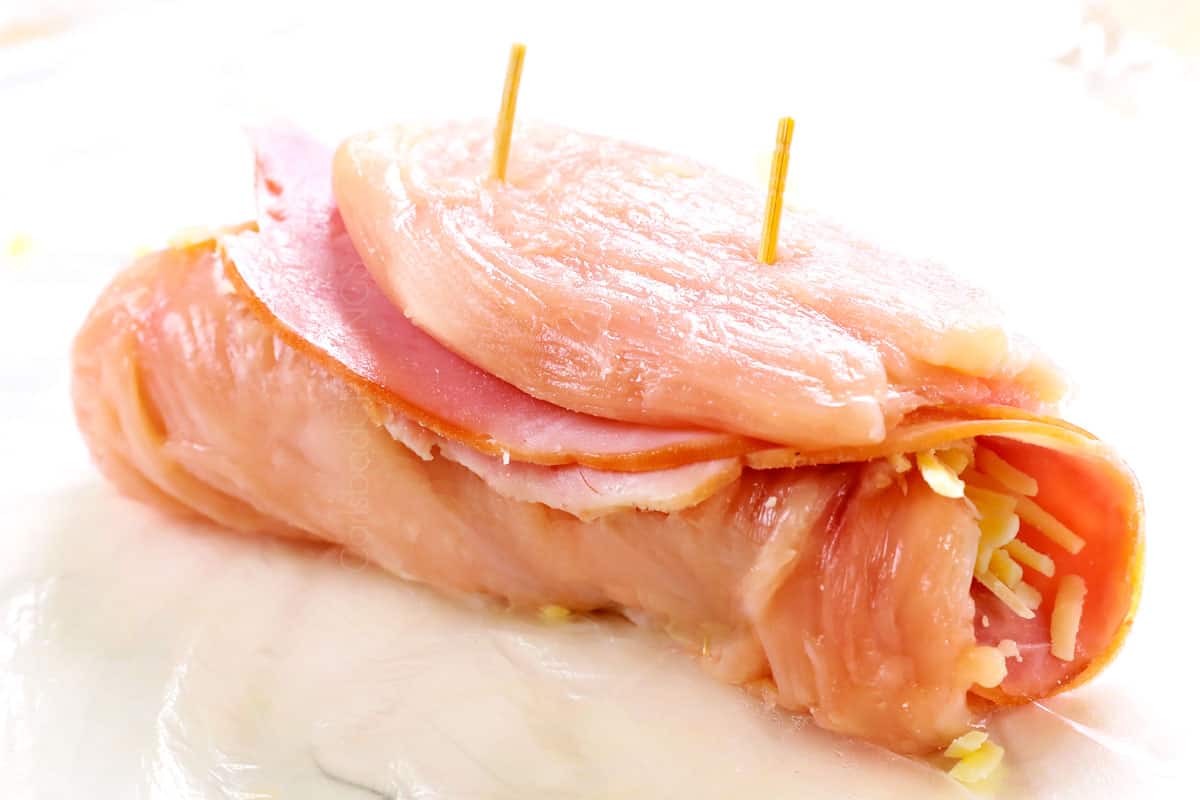 showing how to make chicken cordon bleu recipe by securing the rolled chicken with toothpicks