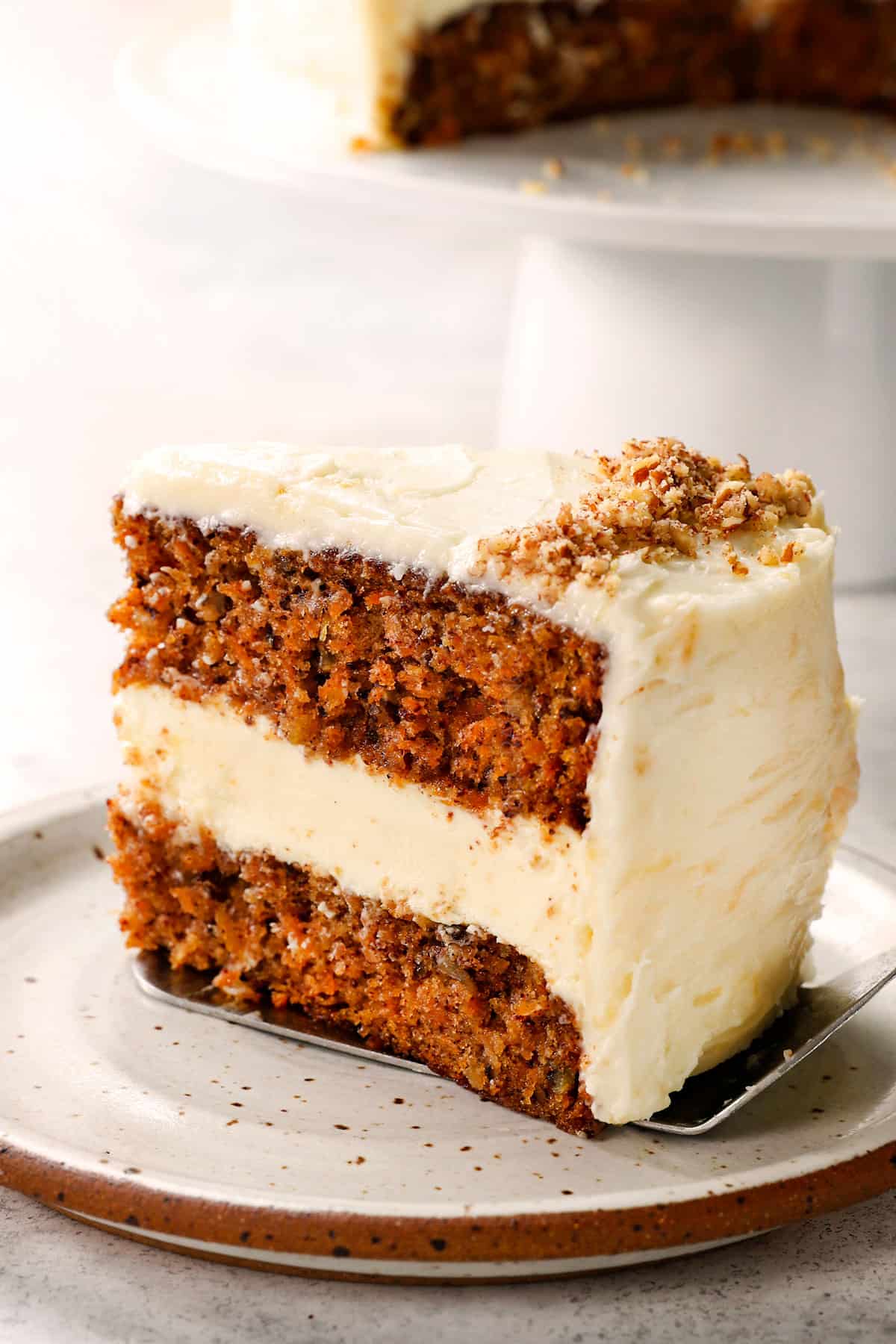 a slice of carrot cake cheesecake on a plate with pineapple and pecans
