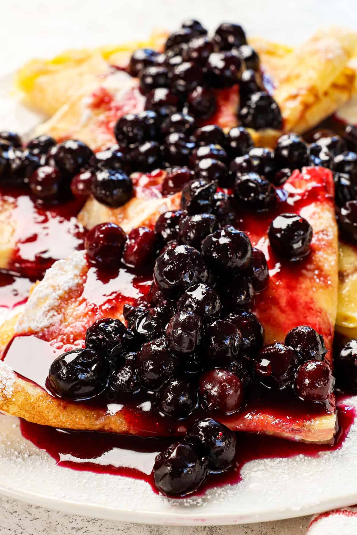 serving crepes with berries, cream and powdered sugar