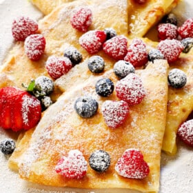 serving crepes with berries, cream and powdered sugar