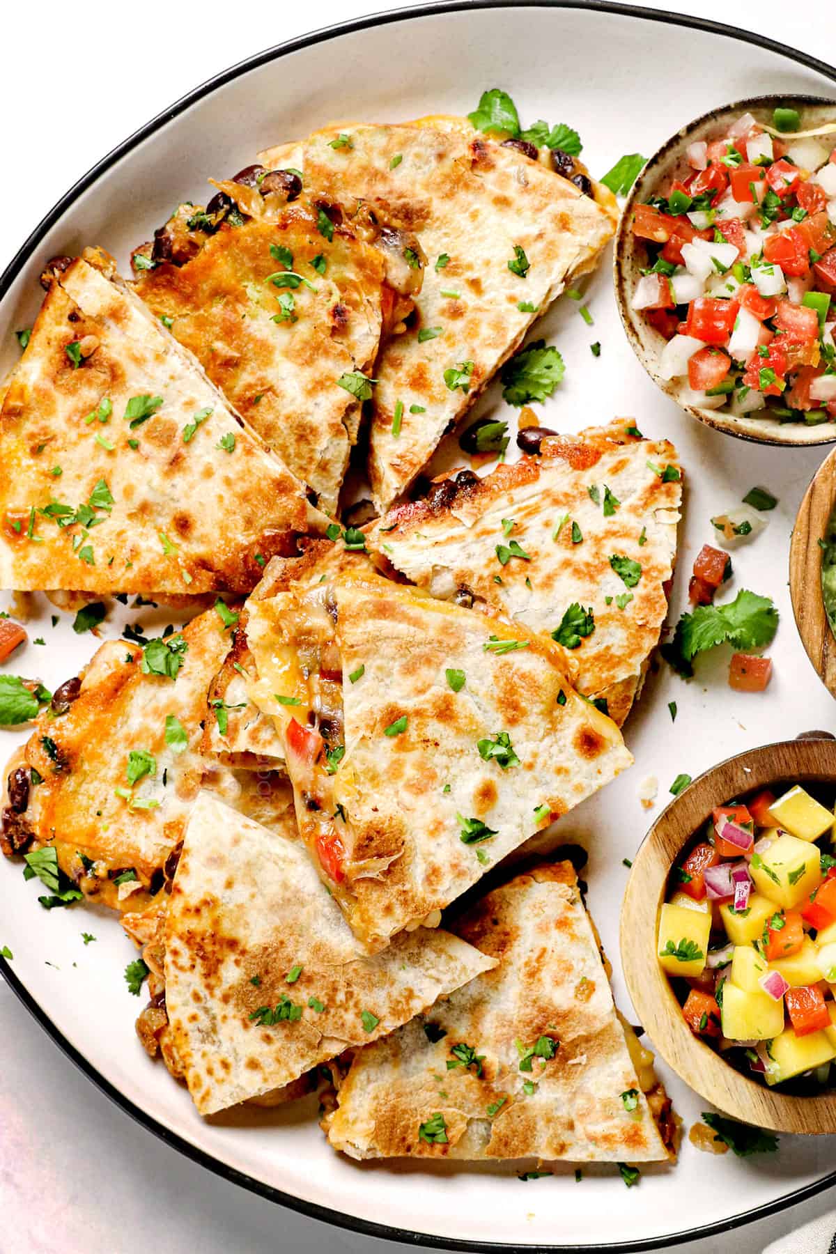 showing how to serve chicken quesadillas recipe by slicing into wedges and serving with pico de gallo, salsa and guacamole on a platter
