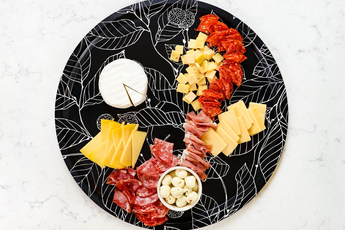 showing how to make a charcuterie board by adding the meats (salami, coppa and prosciutto) to the board around the cheeses