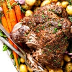 showing how to serve roast leg of lamb on a platter with carrots and potatoes