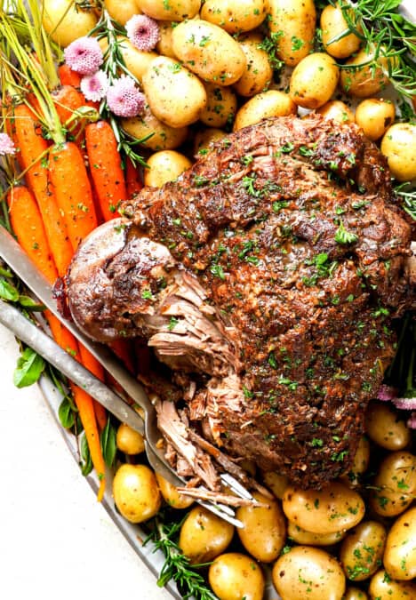 showing how to serve roast leg of lamb on a platter with carrots and potatoes