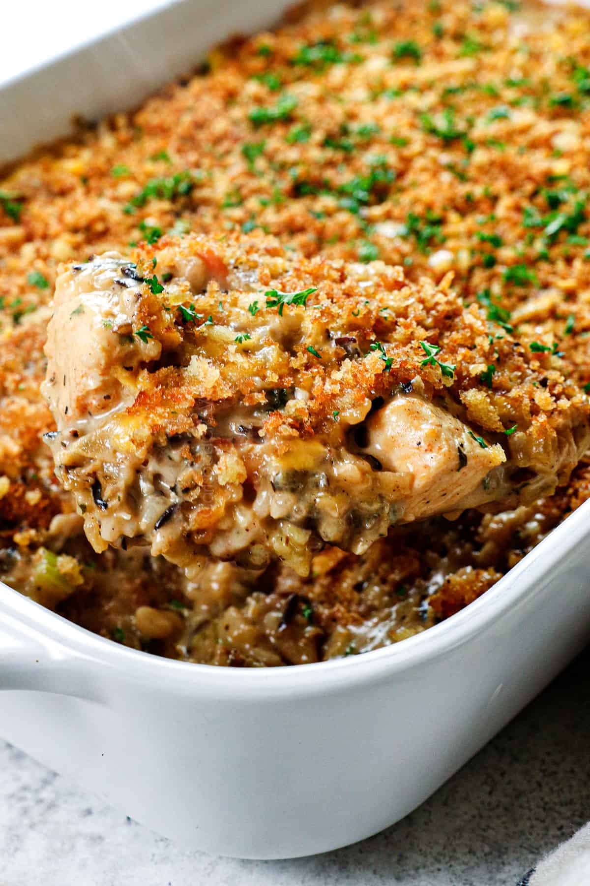 scooping up chicken and wild rice casserole recipe showing all of the ingredients and how creamy it is