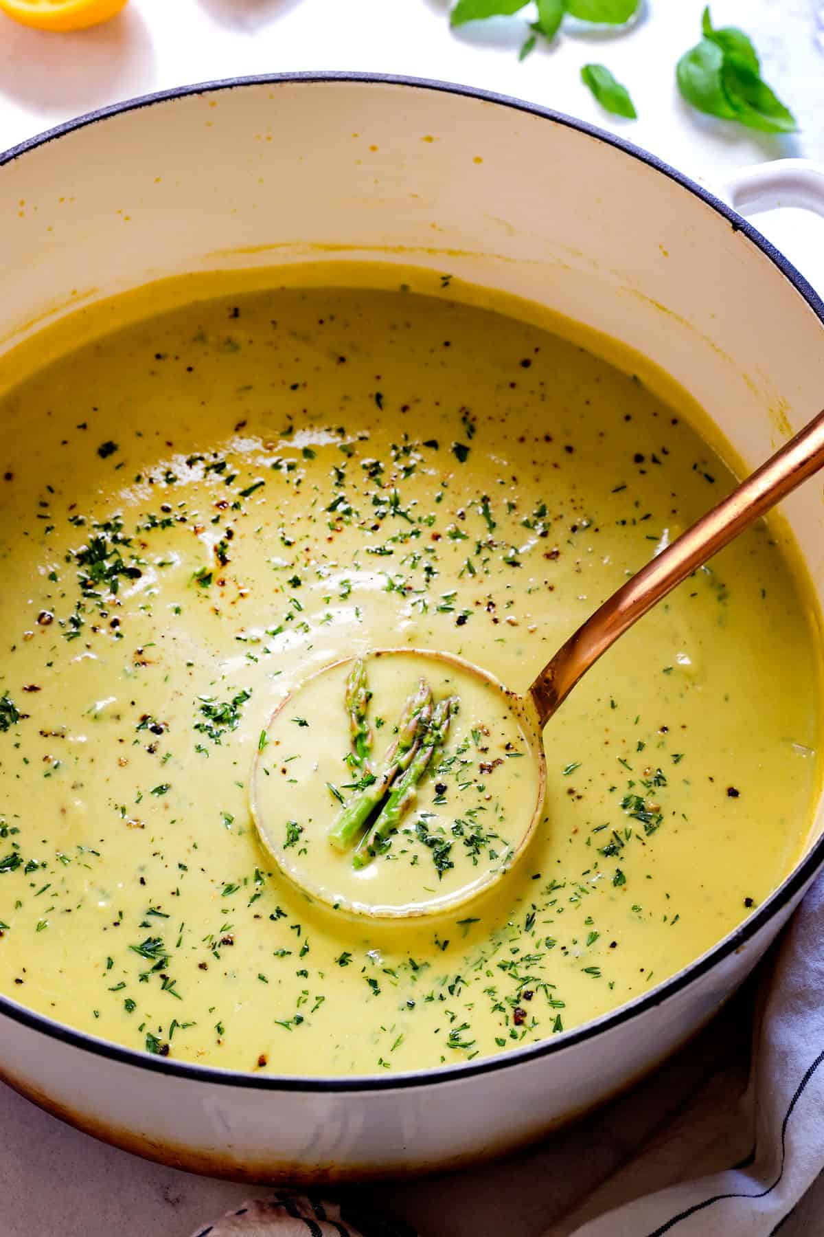 Serving Cream of Asparagus Soup in a pot garnished by fresh herbs