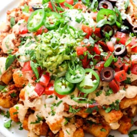 showing how to serve totchos (tater tot nachos) by adding to a platter and garnishing with cilantro, jalapenos and pico de gallo
