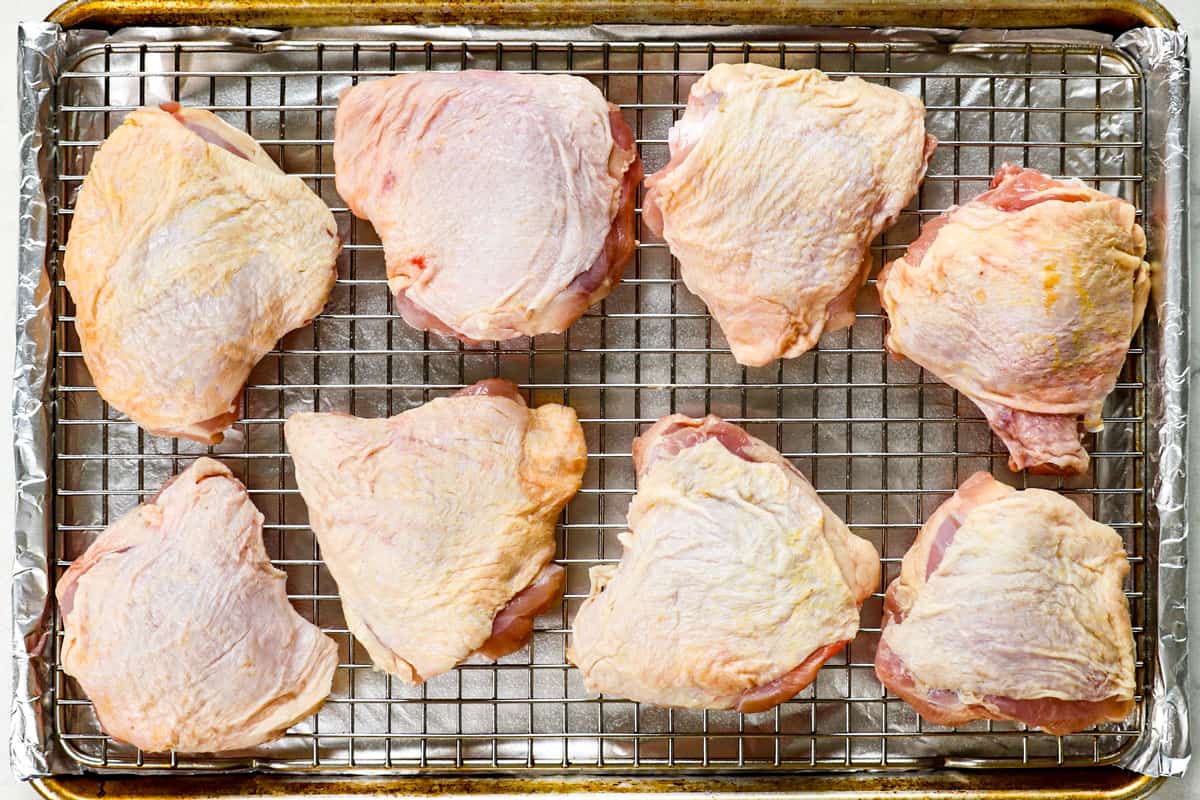 showing how to bake chicken thighs by adding chicken to a baking rack placed on a baking sheet