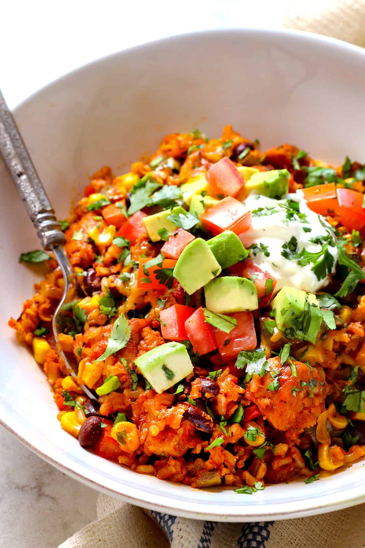 showing how to serve chicken fiesta recipe by adding to a bowl with chopped avocados and sour cream and cilantro