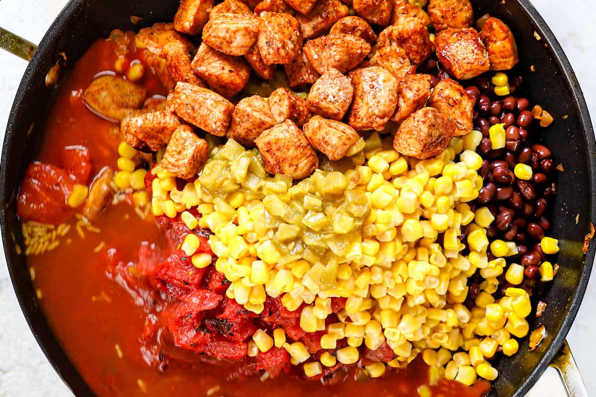 showing how to make fiesta chicken recipe by adding chicken, rice, black beans, corn, bell peppers and enchilada sauce to the skillet to simmer all together