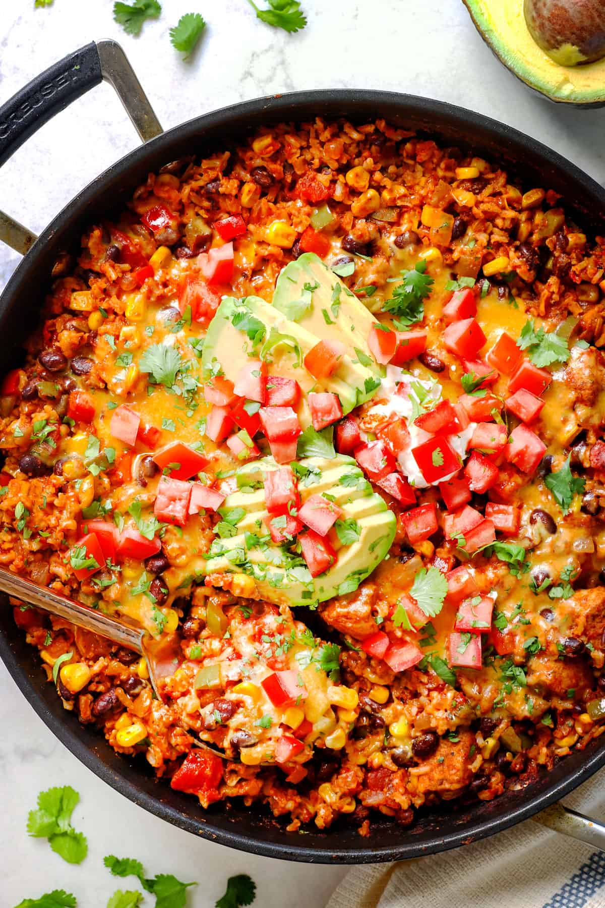 showing how to make chicken fiesta recipe by topping the skillet with sour cream, avocados and pico de gallo