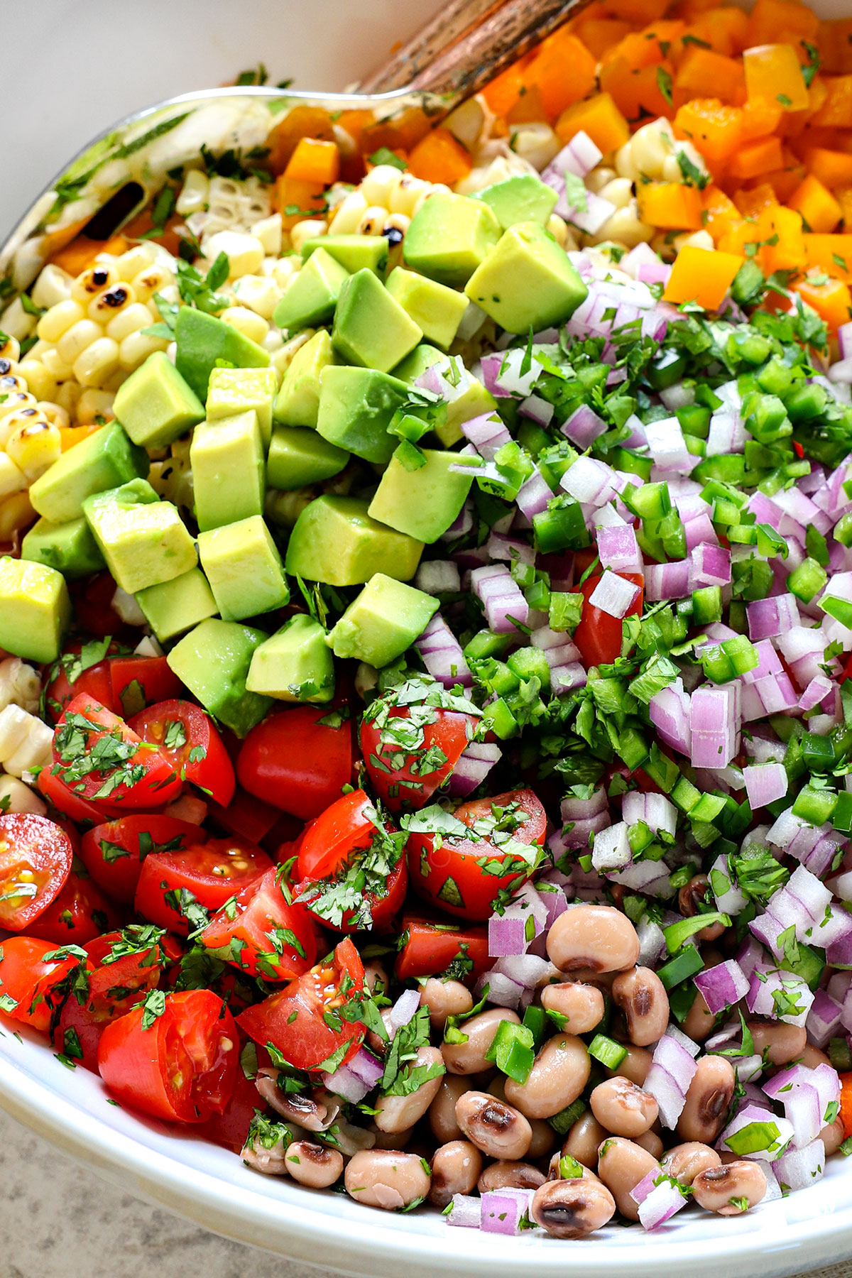 showing the ingredients for ultimate cowboy caviar recipe (Texas Caviar recipe) in a bowl with black eyed peas, black beans, avocados, tomatoes, corn, red onion and cilantro