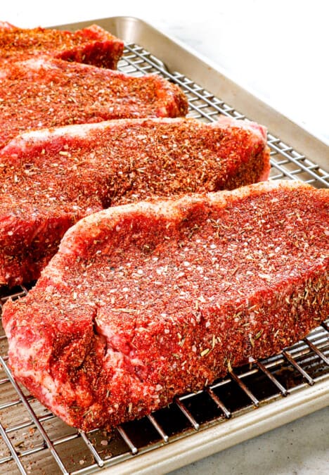 showing how to season steak with steak rub by patting into steaks elevating on a rack