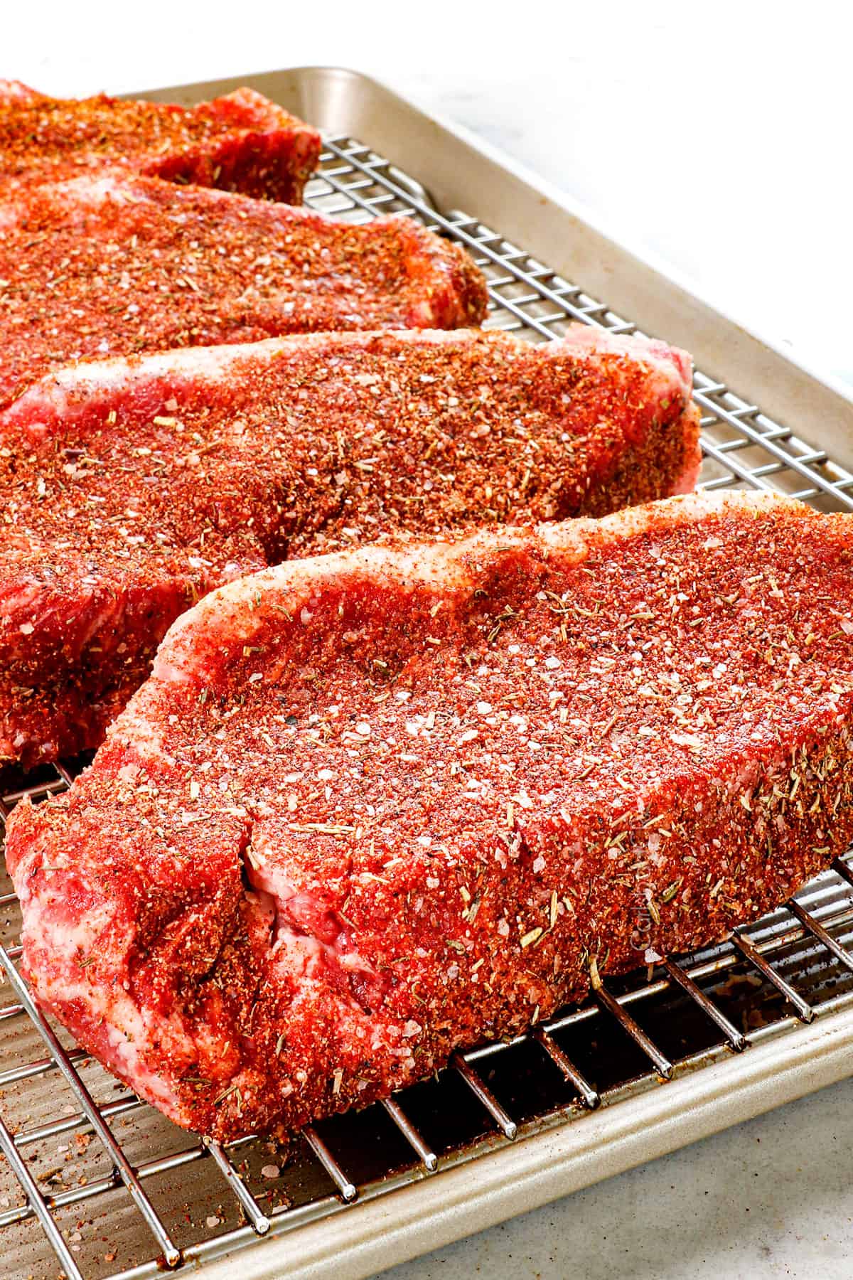 showing how to season steak with steak rub by patting into steaks elevating on a rack