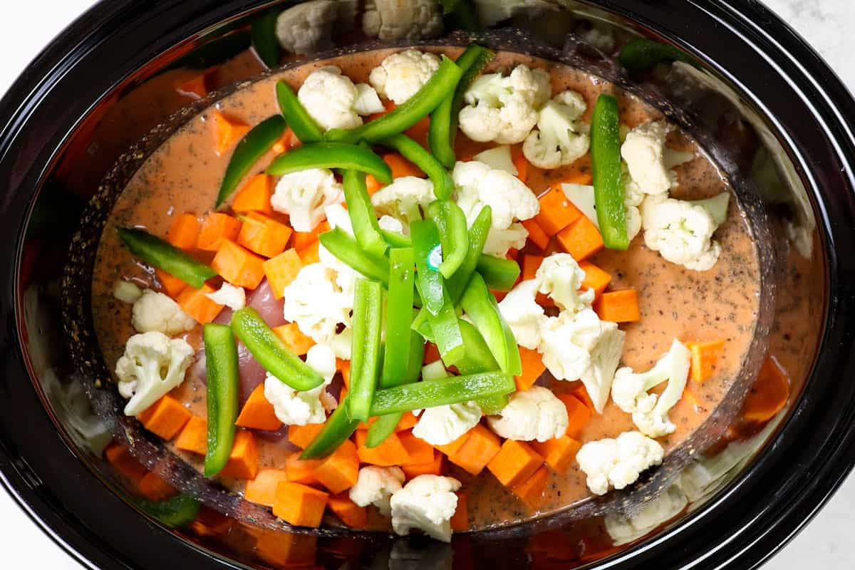 showing how to make crockpot curry chicken by adding chicken thighs, sweet potatoes, cauliflower and bell peppers to the slow cooker with the curry coconut sauce