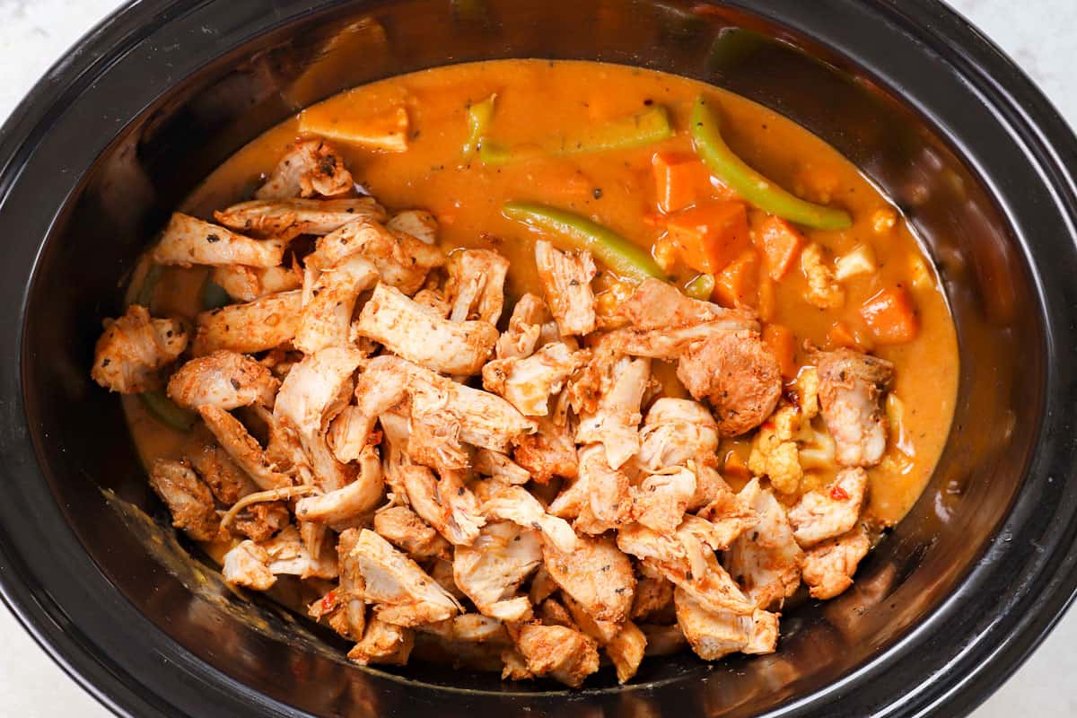 showing how to make crockpot Thai curry chicken by adding the shredded chicken back to the crockpot