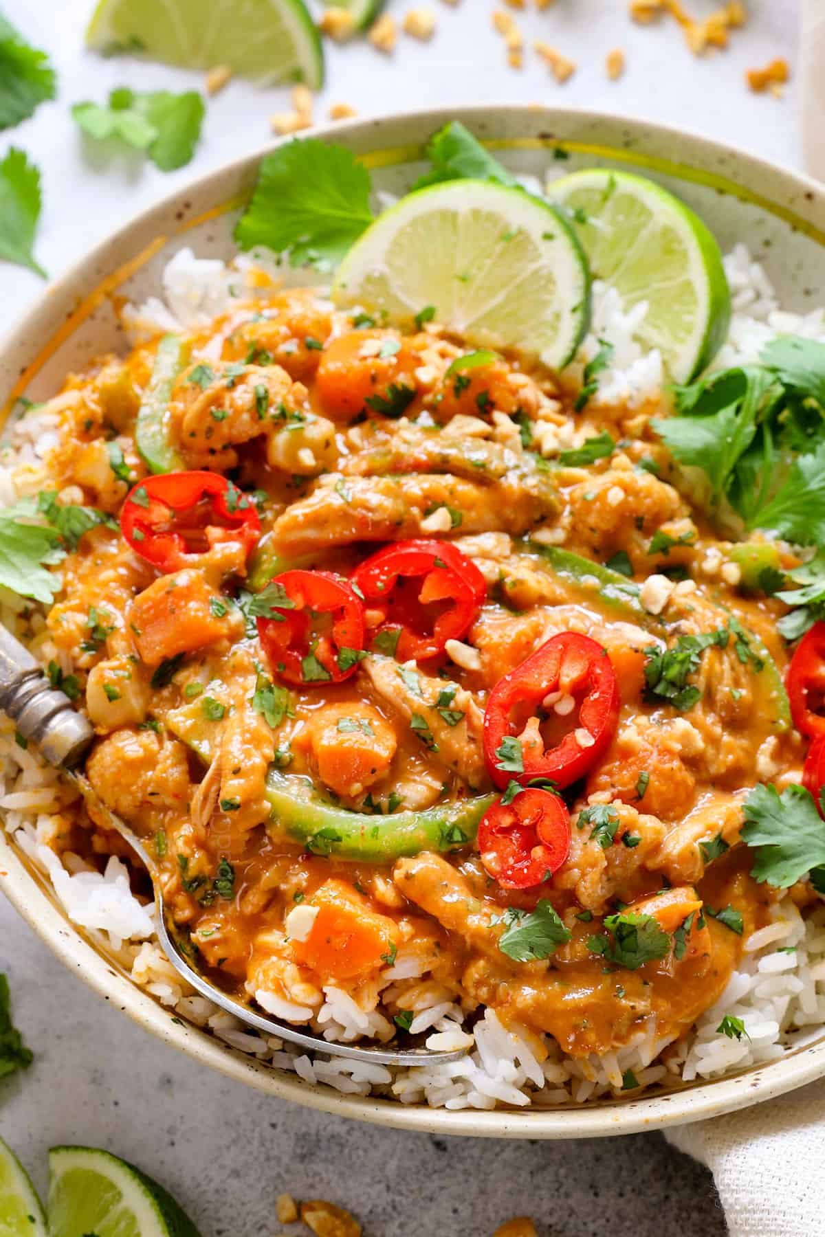 showing how to serve Thai crockpot coconut curry chicken by adding to a bowl with rice and garnishing with cilantro, limes, red chilies