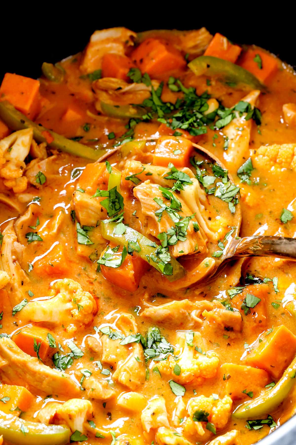 scooping crockpot curried chicken with tender shredded chicken, sweet potatoes, cauliflower and bell peppers