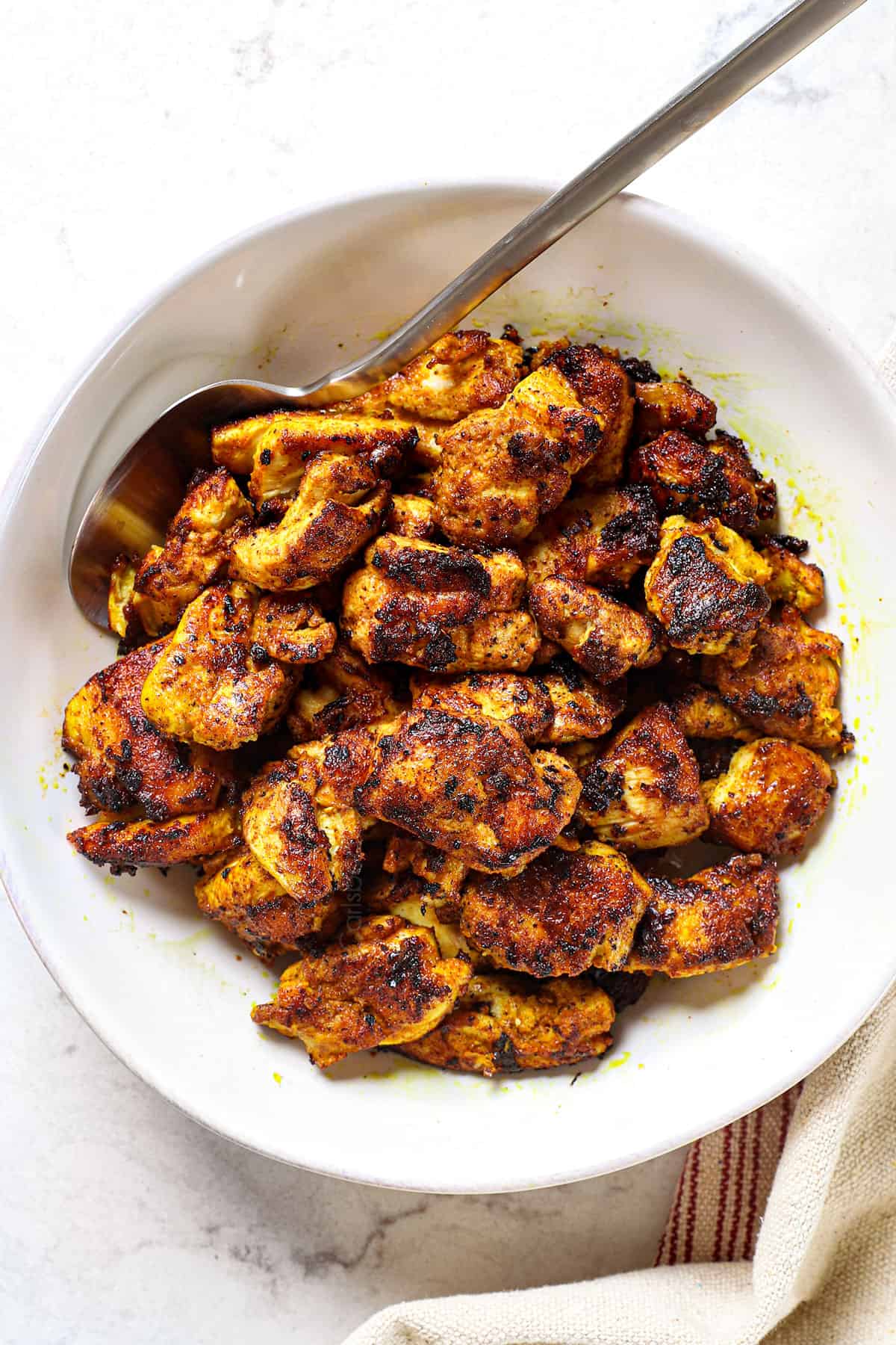 adding Butter chicken to a bowl showing the chargrilled chicken