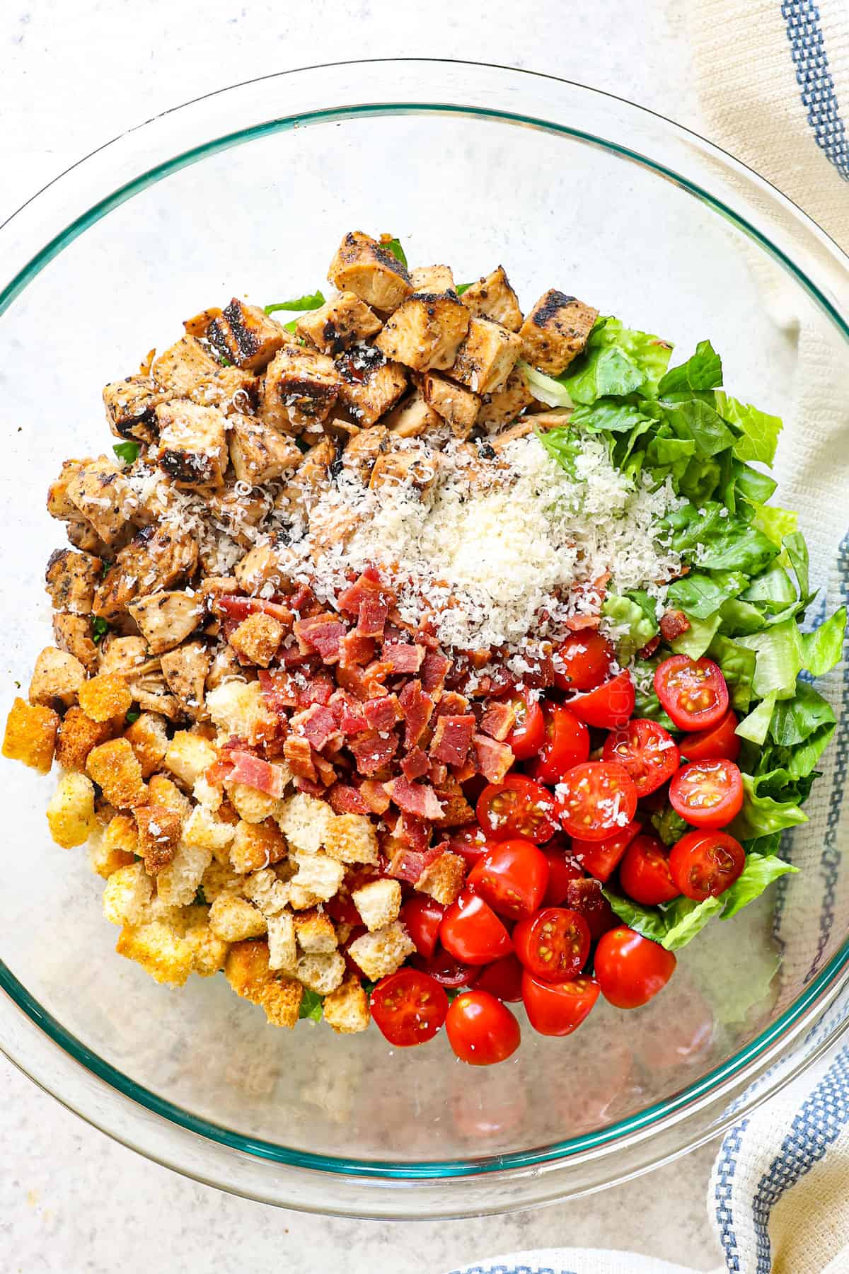 showing how to make chicken Caesar wraps by adding grilled chicken, Romaine lettuce, tomatoes, bacon, Parmesan cheese and croutons to a bowl
