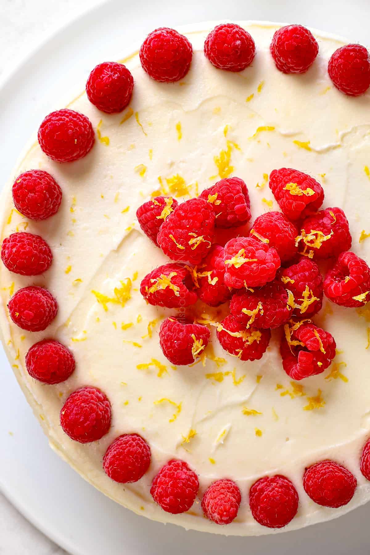 showing how to decorate Raspberry Lemon Cake by adding raspberries to the border and center of the top of the cake