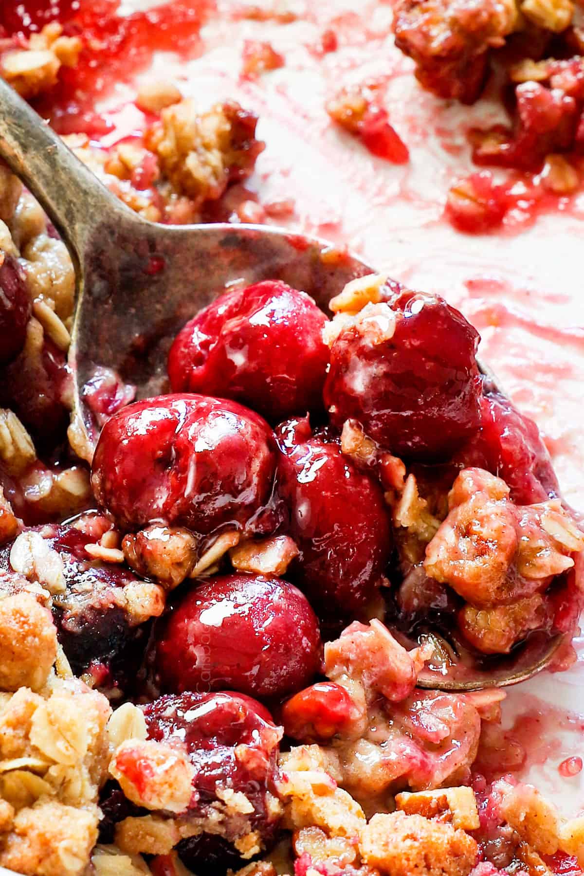 up close of a spoon serving cherry crisp with fresh cherries showing how saucy it is