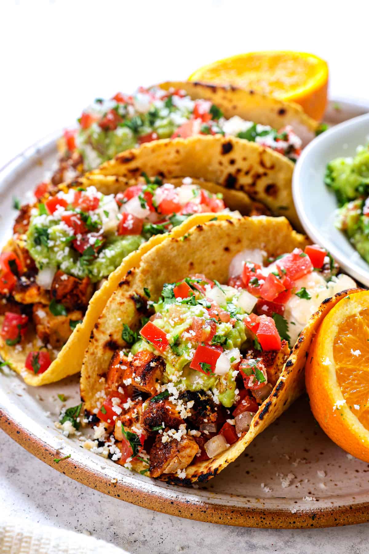 showing how to make chicken street tacos by adding chicken, guacamole and pico de gallo to a small corn tortilla