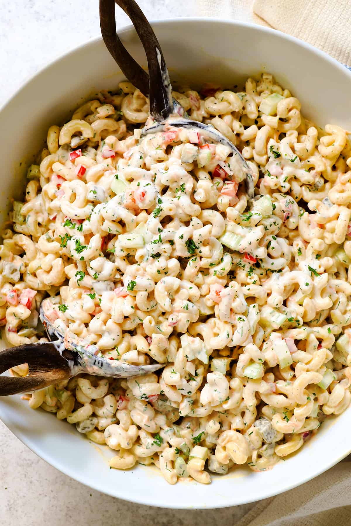 showing how to make macaroni salad recipe by tossing the salad dressing with the salad ingredients until creamy