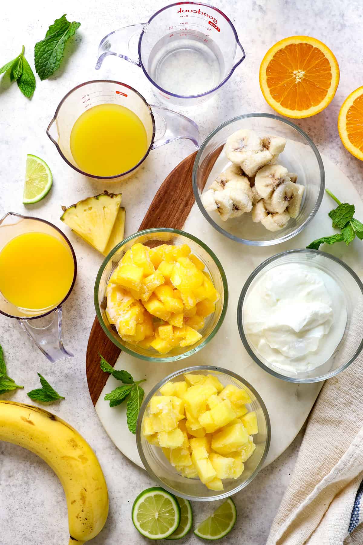 Top view showing ingredients for Tropical Smoothie recipe:  pineapple, mangos, banana, vanilla yogurt, pineapple juice, orange juice and coconut water
