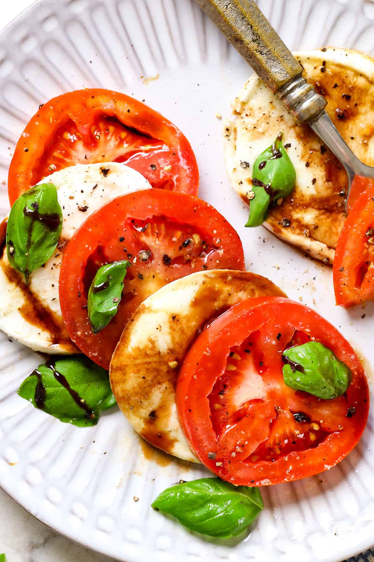 showing how to serve Caprese Salad recipe by adding tomatoes and mozzarella to a plate with basil