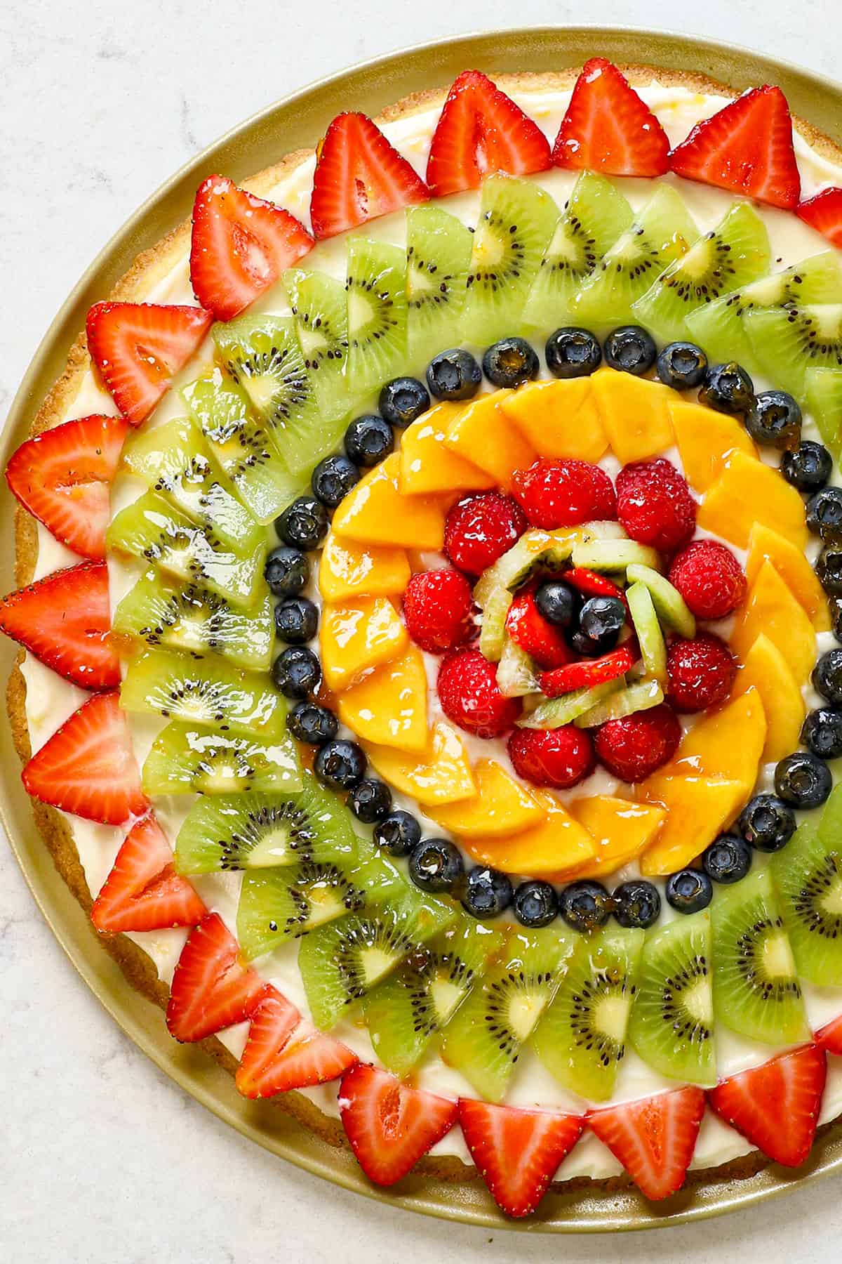 showing how to make fruit pizza by adding fruit in a pattern over cream cheese frosting