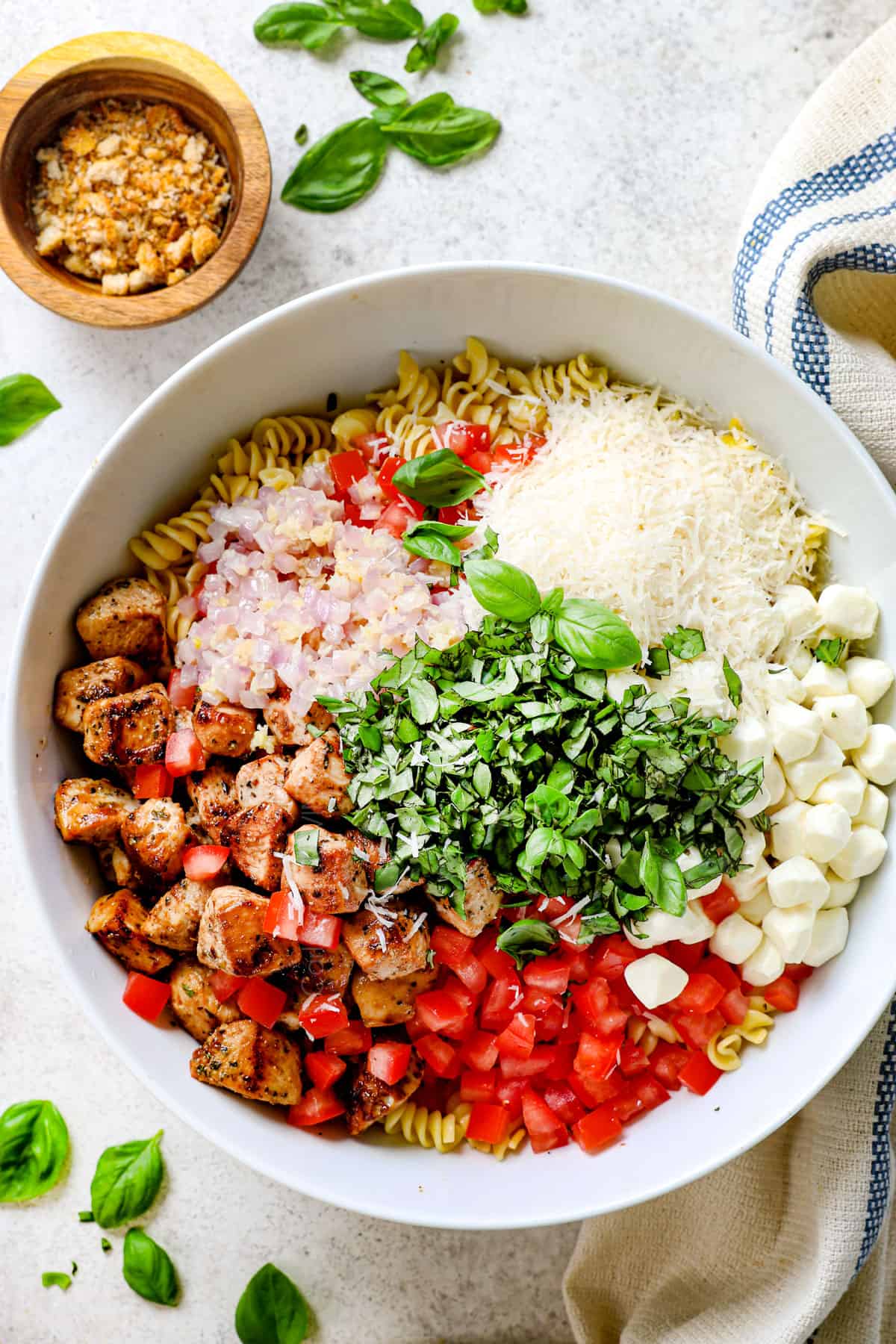 showing chicken pasta salad ingredients in a bowl:  pasta, chicken, tomatoes, basil, onions, garlic, parmesan and mozzarella 