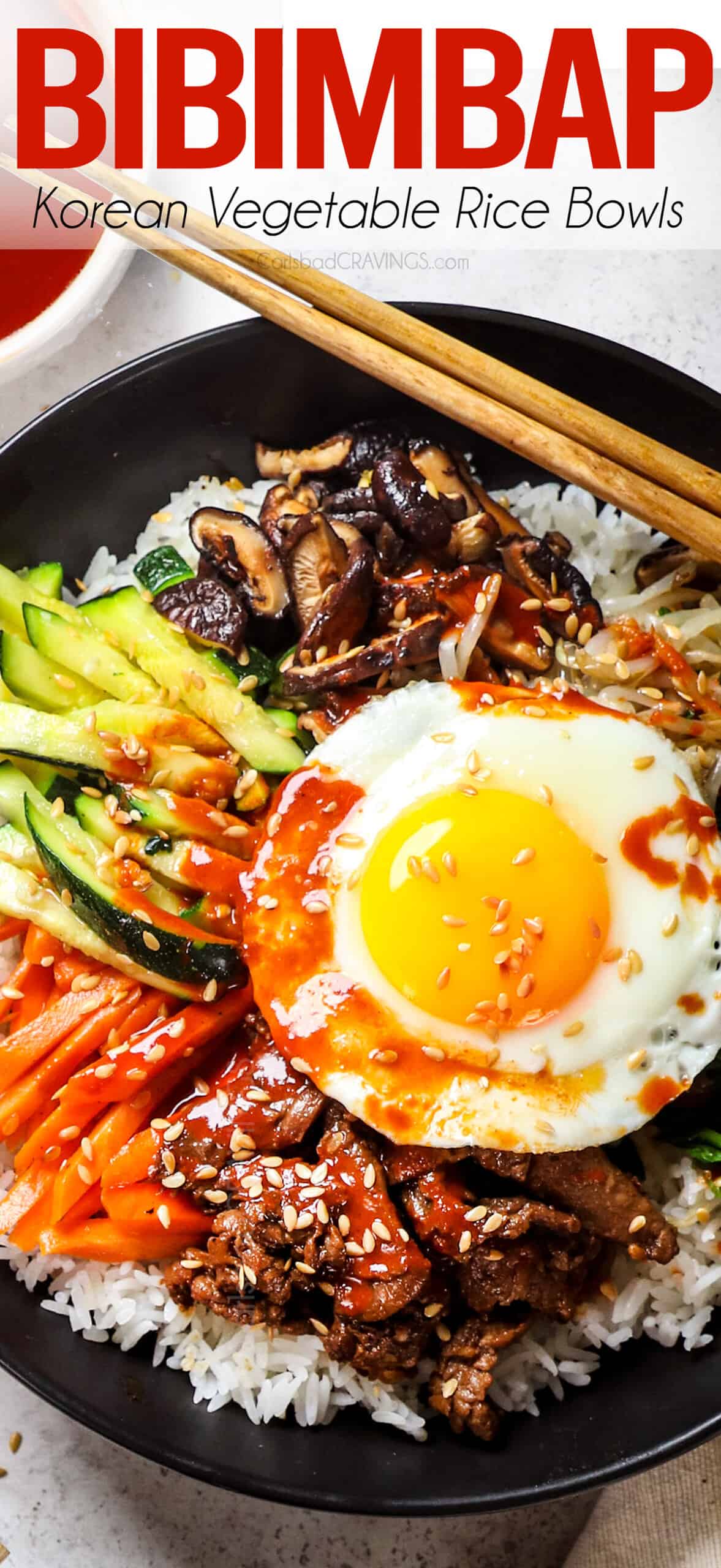 top view of bibimbap (Korean Rice Bowl) with carrots, zucchini, spouts, mushrooms, egg, Korean beef and bibimbap sauce