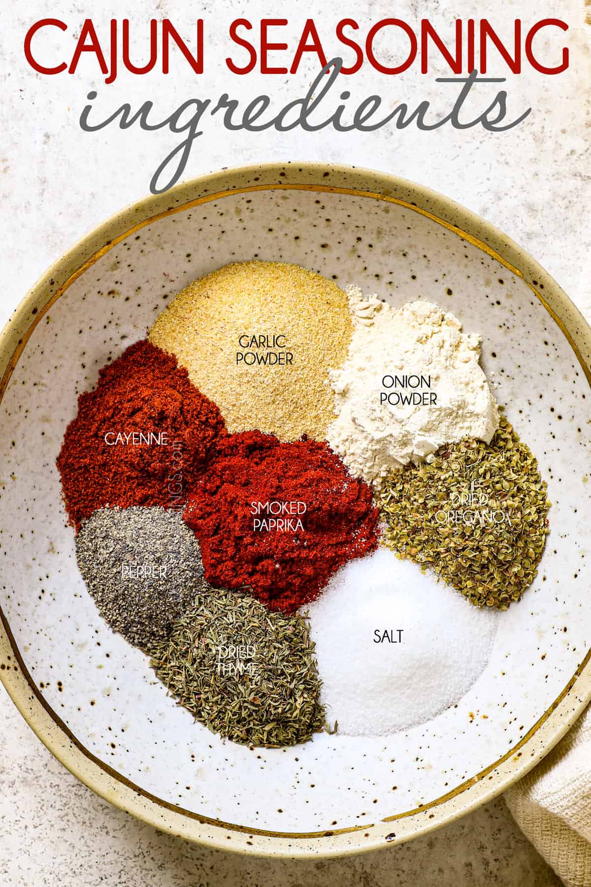 top view of Cajun seasoning recipe ingredients in a bowl:  salt, garlic powder, onion powder, smoked paprika, pepper, cayenne pepper, oregano and thyme
