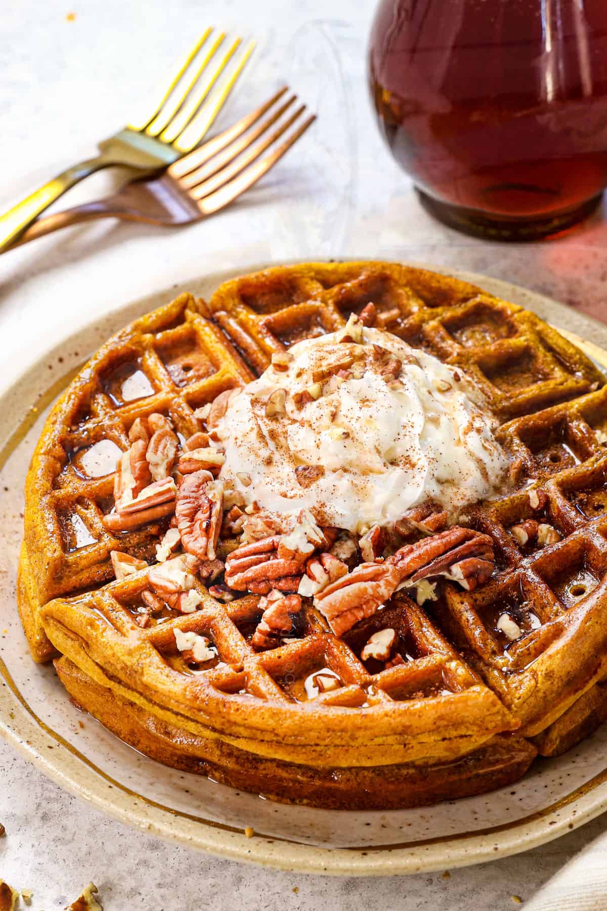 pumpkin waffles being served on a plate with syrup, whipped cream and pecans
