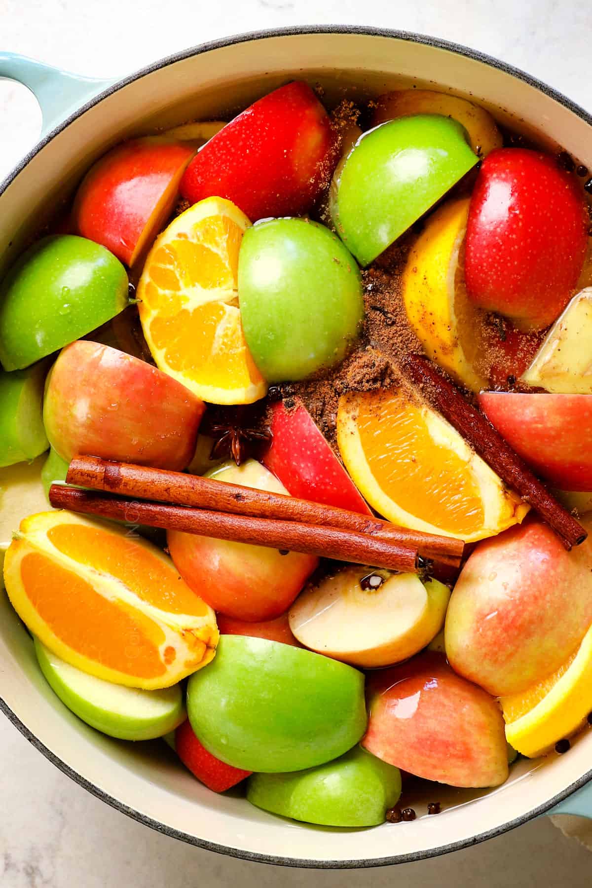 showing how to make apple cider recipe by adding apples, oranges, cinnamon, cloves, ginger and water to a large pot