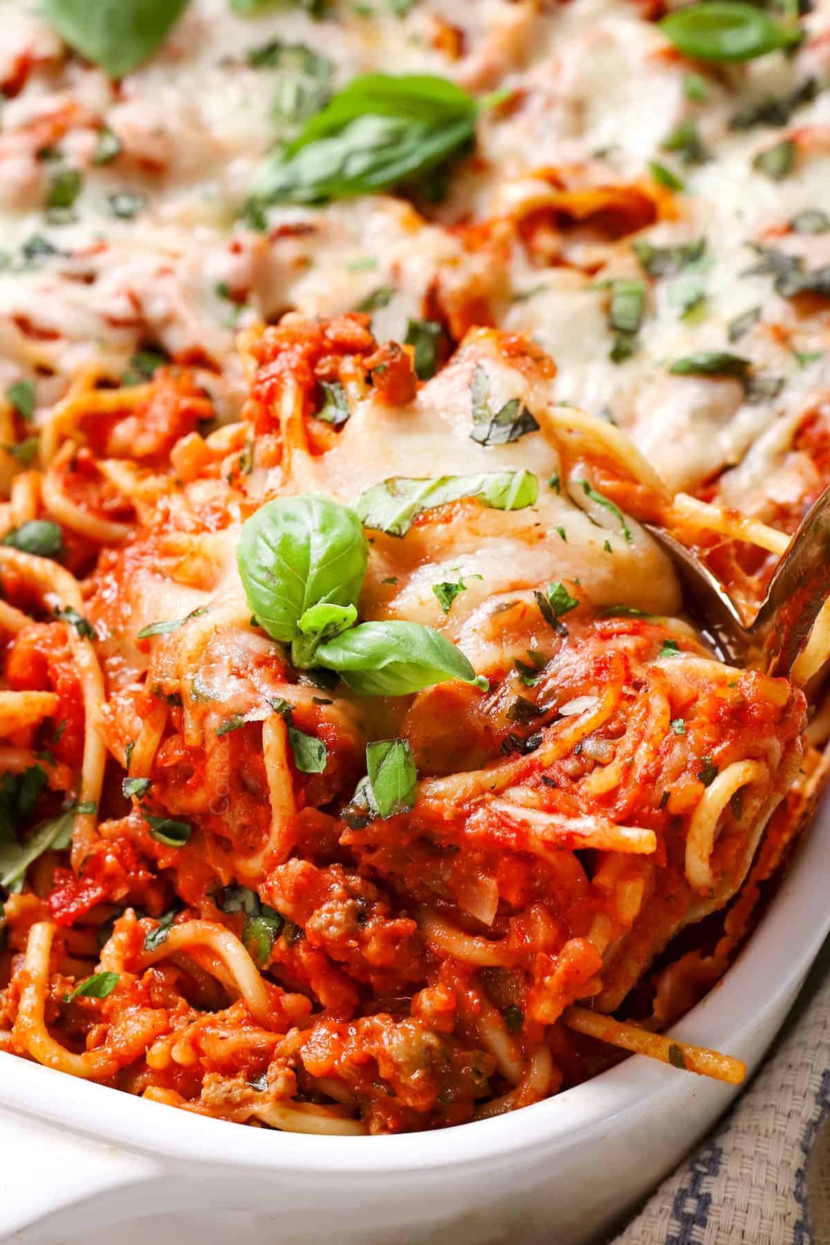 up close of serving baked spaghetti casserole garnished by basil